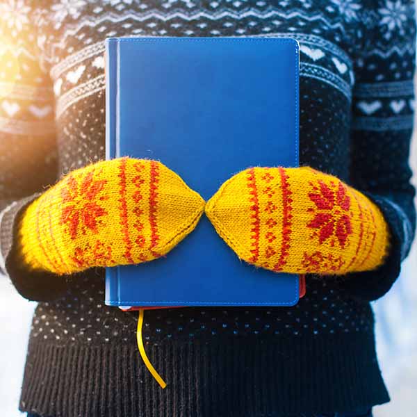 A person wearing yellow and red mittens with their hands wrapped around a blue book